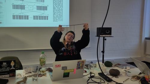 Someone holding up a khipu with explanation of meanings of knots being projected behind them.